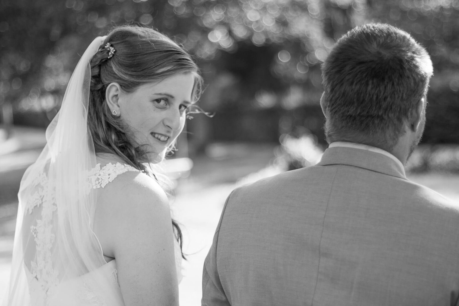 Frau im Hochzeitskleid steht neben Ehemann im Anzug und schaut nach hinten